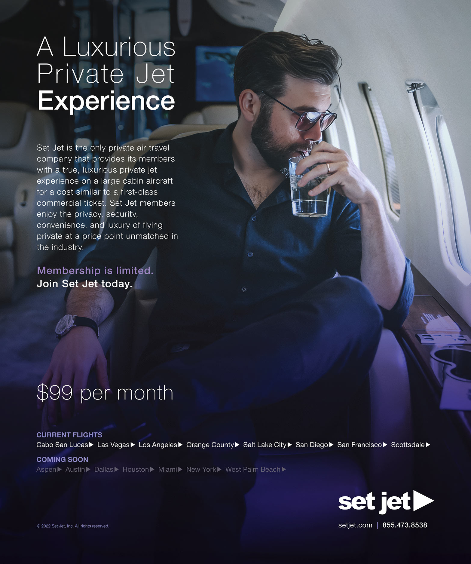 A bearded man in sunglasses relaxing and having a drink inside a private jet cabin.